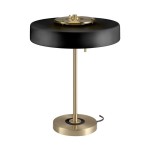 Lampa stołowa Artdeco z trzema gniazdami E14, w kolorze złotym szczotkowanym i czarnym. Okrągła podstawa, smukły stelaż, czarny abażur. Ujęcie z boku, prezentujące detale konstrukcji oraz włącznik. Tło neutralne, podkreślające elegancję lampy.