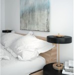 Lampa stołowa Artdeco 3xE14 w kolorze złotym szczotkowanym i czarnym, umieszczona obok łóżka. Lampa ma okrągły klosz, metalową podstawę oraz elegancki design, idealna do nowoczesnych wnętrz. W tle widoczne białe poduszki i abstrakcyjny obraz na ścianie.