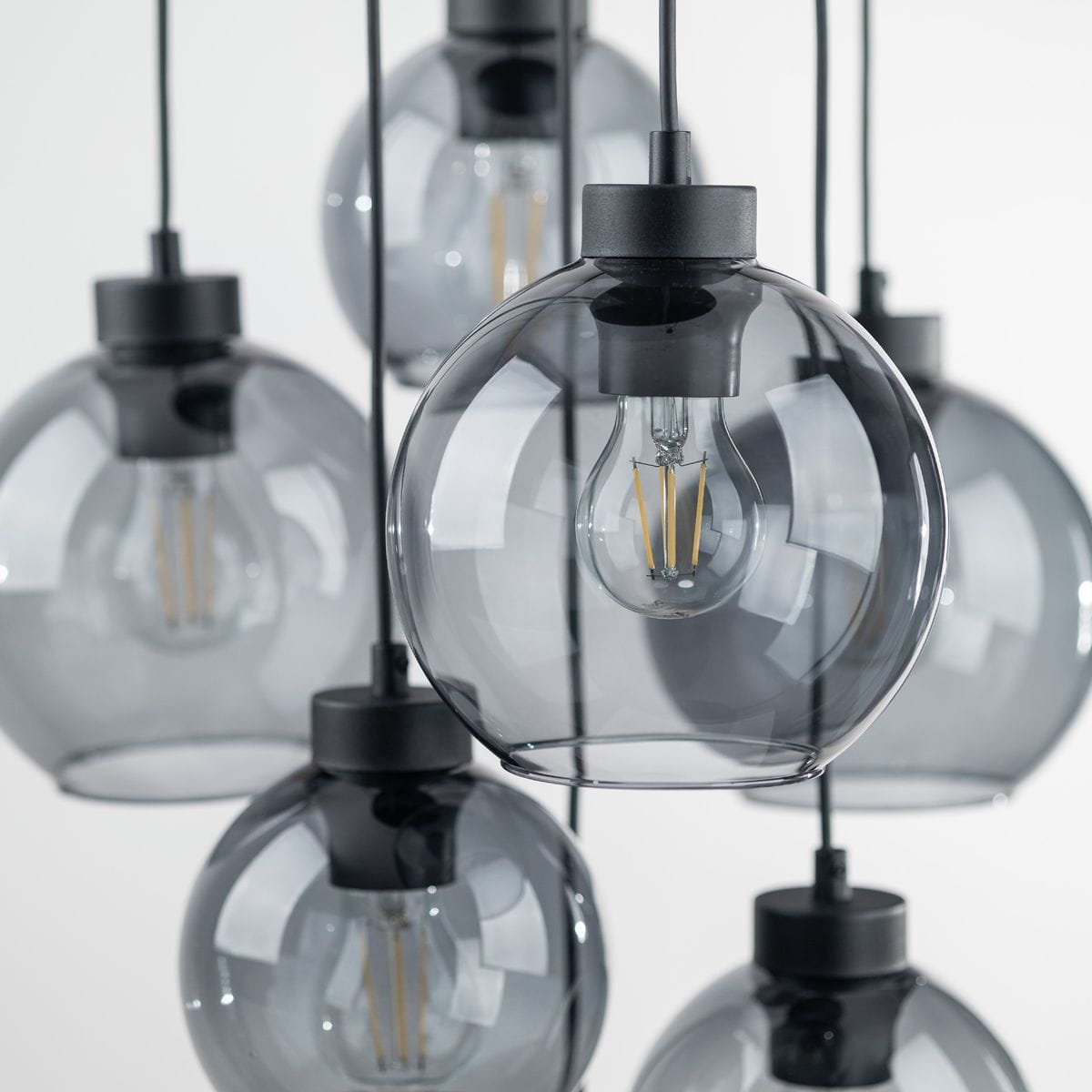 Lampa wisząca Cubus z siedmioma szklanymi kloszami w kolorze grafitowym i czarnymi elementami montażowymi. Klosze mają okrągły kształt i są zawieszone na cienkich linkach, z widocznymi żarówkami E27. Tło proste, białe.