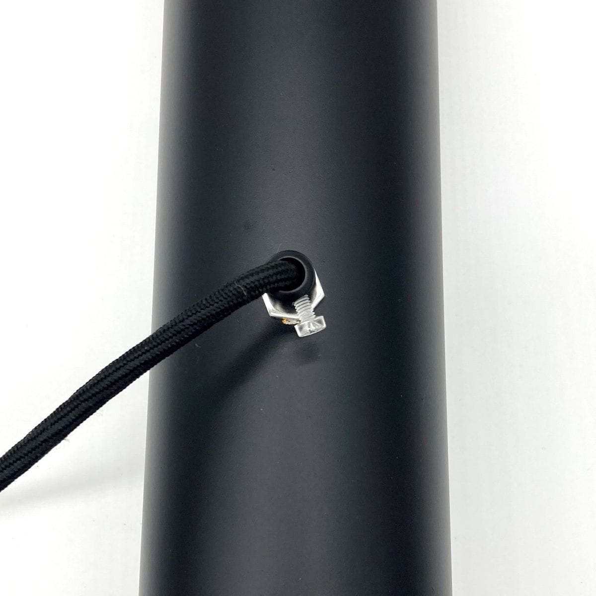 Czarna lampa wisząca Black Tube z dwoma miejscami na żarówki E27. Widać detal mocowania kabla w kolorze srebrnym oraz czarny, matowy korpus lampy. Kąt ujęcia zbliżony na elementy montażowe.