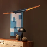 Lampa wisząca Black Tube 2xE27 w kolorze czarnym z złotym wykończeniem, zawieszona na cienkim przewodzie. Widok z przodu, z tłem w odcieniach brązu i niebieskiego, obok drewnianego mebla oraz dekoracji.