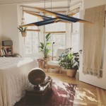 Lampa wisząca Black Tube 2xE27 w kolorze czarnym i złotym, w kształcie podłużnych tub, zawieszona nad przestrzenią z roślinami. Wnętrze jasne, z naturalnym światłem, podłoga drewniana, dekoracje w stylu boho.