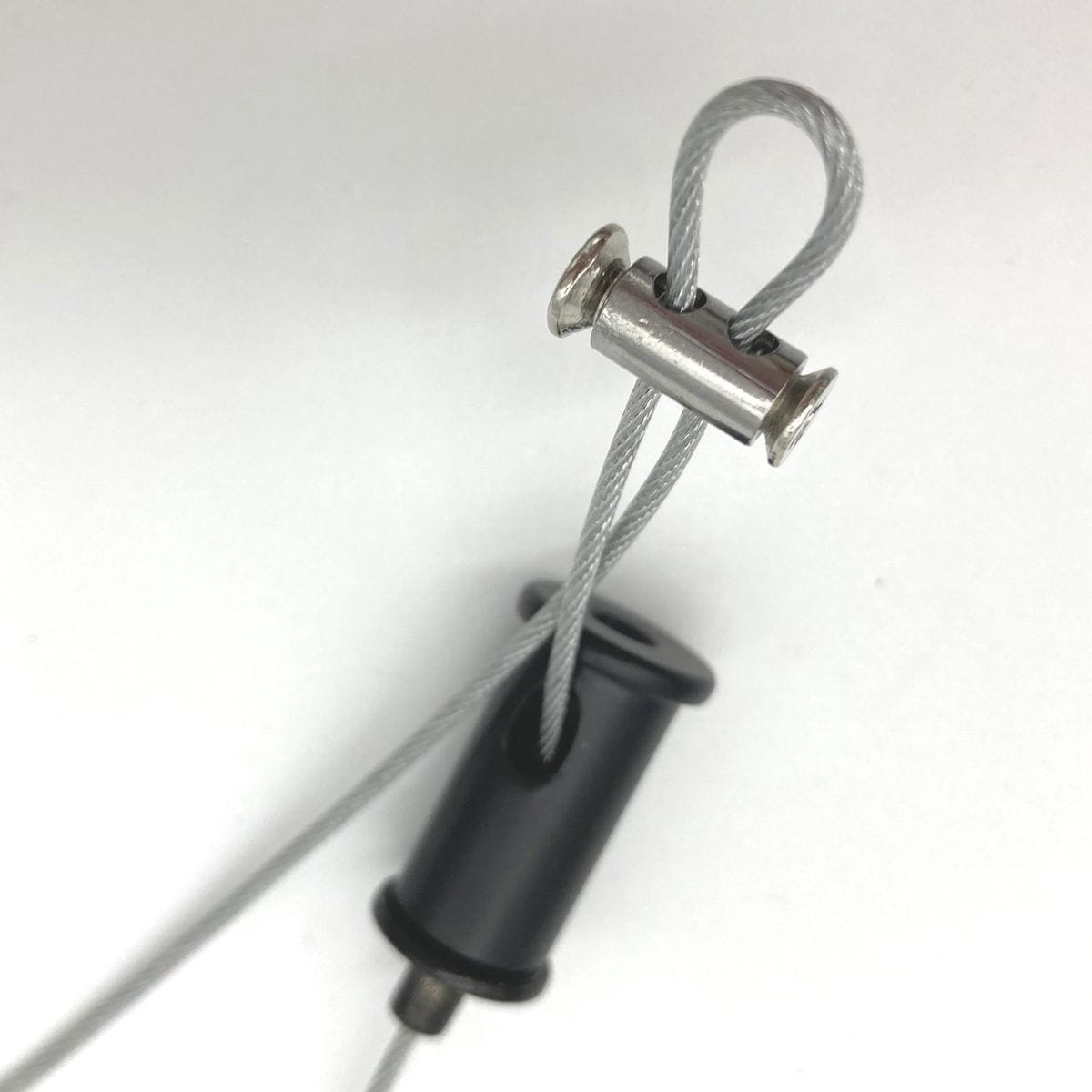 Zbliżenie na element mocujący do lampy wiszącej Black Tube. Widać szary przewód oraz metalowy klips, który trzyma przewód w miejscu. Element jest czarny, wykonany z tworzywa, z widocznym mechanizmem mocującym. Tło jasne, neutralne.