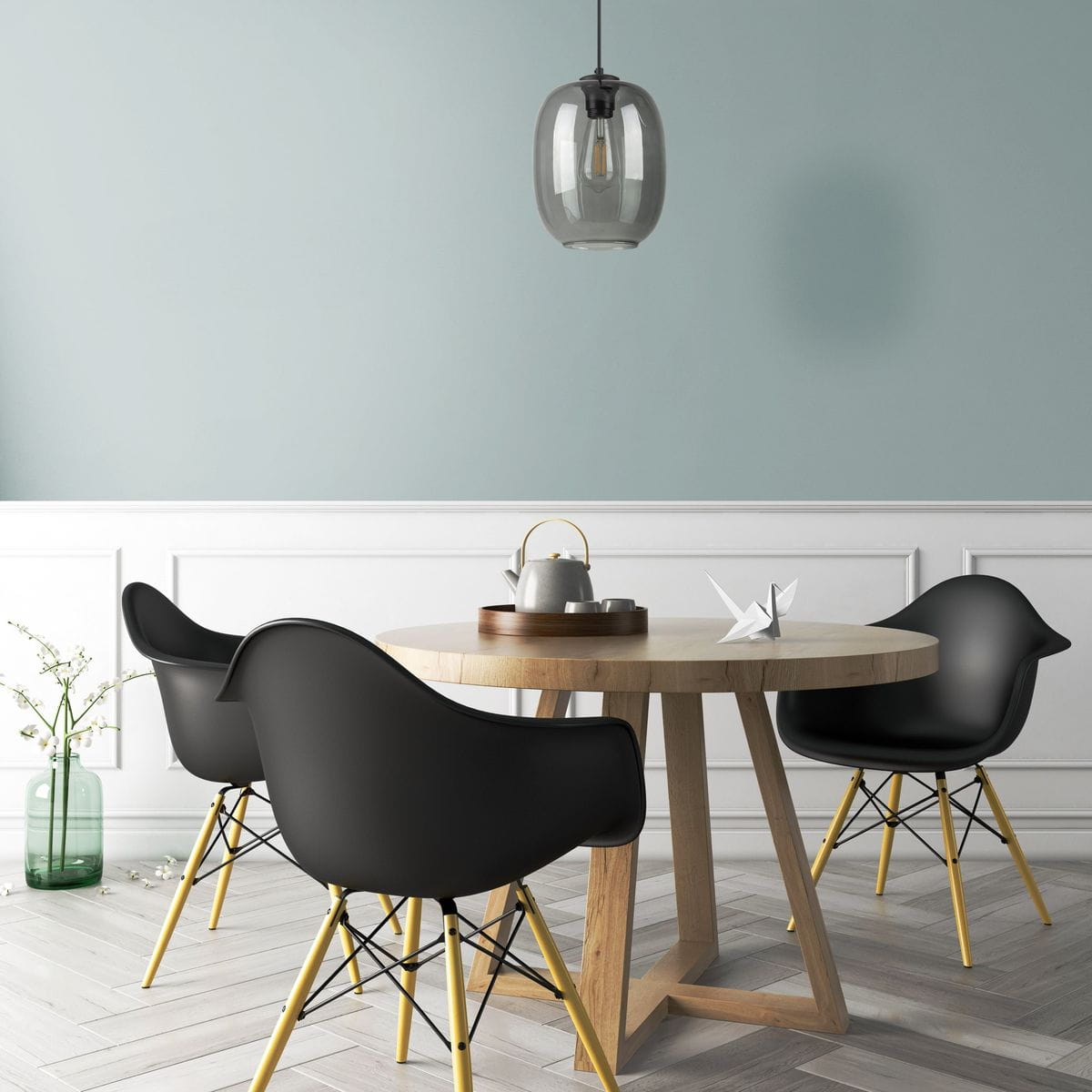 Lampa wisząca Elio 1xE27 w kolorze grafitowym, o zaokrąglonym kształcie, zawieszona nad okrągłym drewnianym stołem. W tle widoczne czarne krzesła i pastelowa ściana. Wnętrze nowoczesne, z dodatkami w jasnych kolorach.