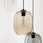 Lampa wisząca Elio z trzema kloszami w odcieniach czerni i multikoloru. Szklane klosze o zaokrąglonym kształcie, w jednej z nich widoczna żarówka E27. Zawieszona na czarnym przewodzie, w tle neutralne, jasne tło.