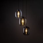 Lampa wisząca Elio z trzema kloszami w kształcie owalnym, wykonanymi z ciemnego szkła, z żarówkami E27. Zawieszona na czarnych przewodach, idealna do nowoczesnych wnętrz. Ujęcie z przodu, na ciemnym tle.