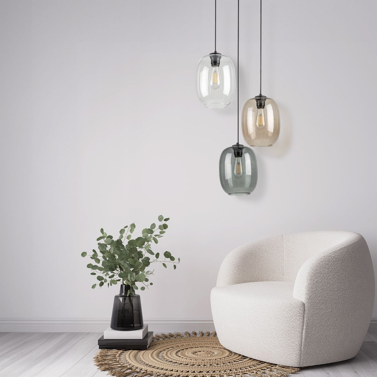 Lampa wisząca Elio 3xE27 w kolorze czarnym z multikolorowymi kloszami (przezroczysty, brązowy, zielony) zwisająca z sufitu. Ustawiona nad jasnym fotelem w kształcie muszli, obok doniczki z eukaliptusem na plecionym dywaniku.