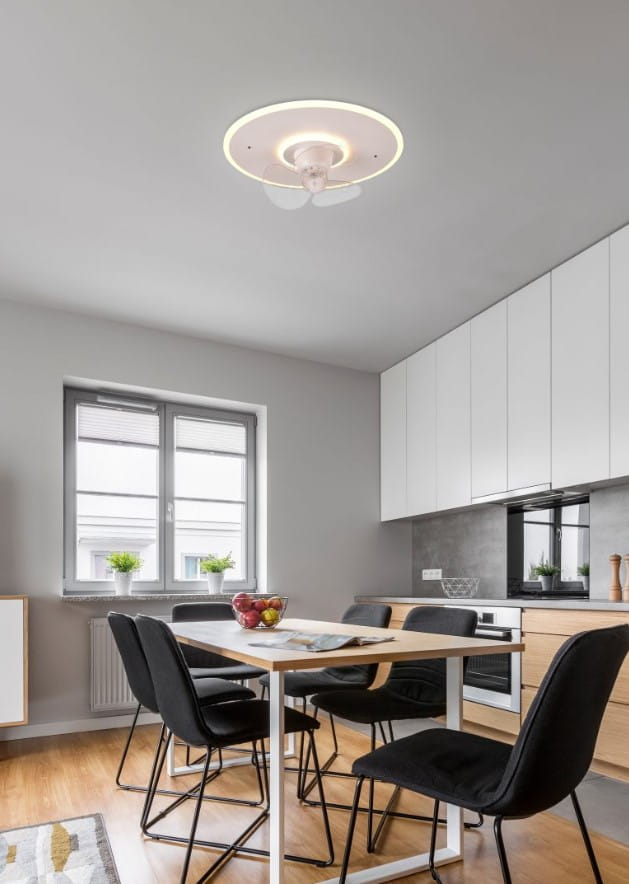 Lampa sufitowa Nybro z wentylatorem, biała, z podświetleniem LED. Zainstalowana na suficie w nowoczesnej kuchni, z widocznymi czterema łopatkami wentylatora. W tle stół z czarnymi krzesłami i oknem.
