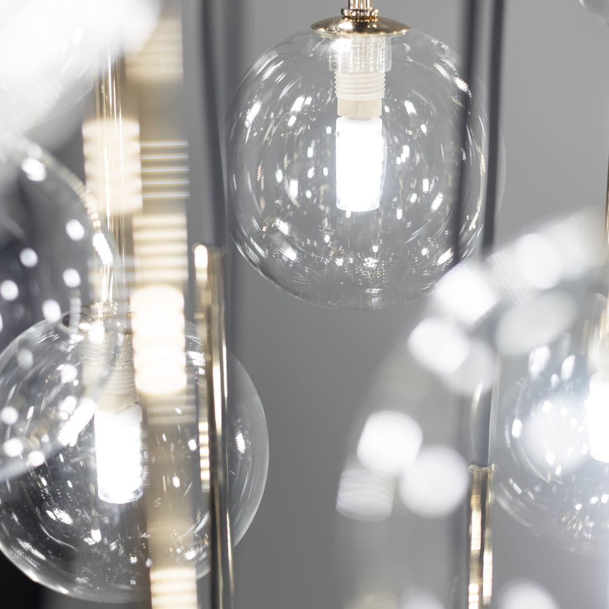 Lampa wisząca Aurora z 16 źródłami światła G9, w czarnej metalowej konstrukcji. Przezroczyste, okrągłe klosze z wykończeniem w połysku, z widocznymi żarówkami LED. Ujęcie zbliżeniowe na detale kloszy i mocowania.