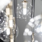 Lampa wisząca Aurora z 16 źródłami światła G9, w czarnej metalowej konstrukcji. Przezroczyste, okrągłe klosze z wykończeniem w połysku, z widocznymi żarówkami LED. Ujęcie zbliżeniowe na detale kloszy i mocowania.