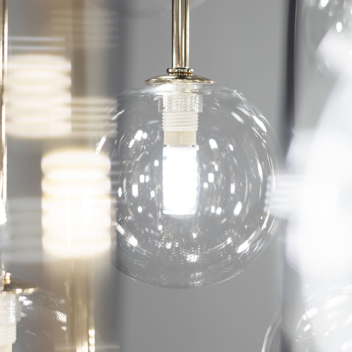 Lampa wisząca Aurora z 16 żarówkami G9, w czarnej i przezroczystej obudowie. W zbliżeniu widoczne szklane klosze oraz źródła światła, zawieszone na metalowej konstrukcji. Tło w odcieniu szarym, co podkreśla elegancję lampy.