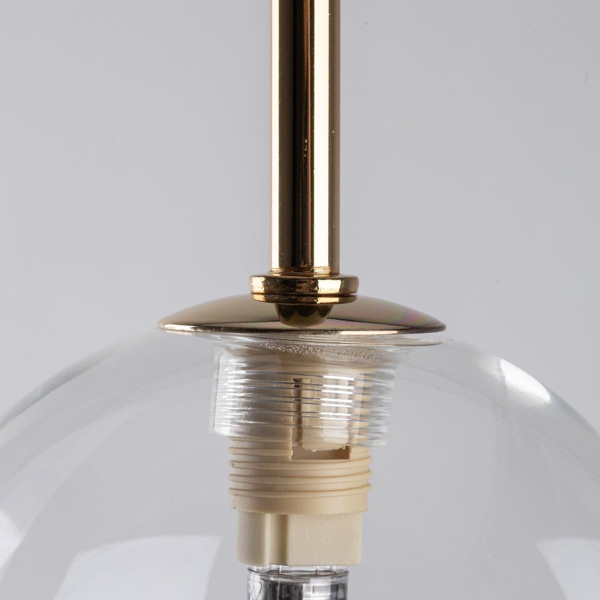 Lampa wisząca Aurora w kolorze czarnym i transparentnym, z metalowym, złotym uchwytem. Ujęcie z bliska na elementy montażowe przy górnej części lampy, z widoczną oprawką G9. Szklana kula lampy częściowo odsłonięta.