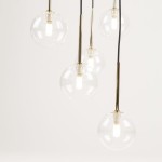 Lampa wisząca Aurora z sześcioma kulistymi kloszami z przezroczystego szkła na złotych metalowych podstawkach, zwisająca na czarnych przewodach. Klosze mają widoczne źródła światła G9. Tło jasne, jednolite.