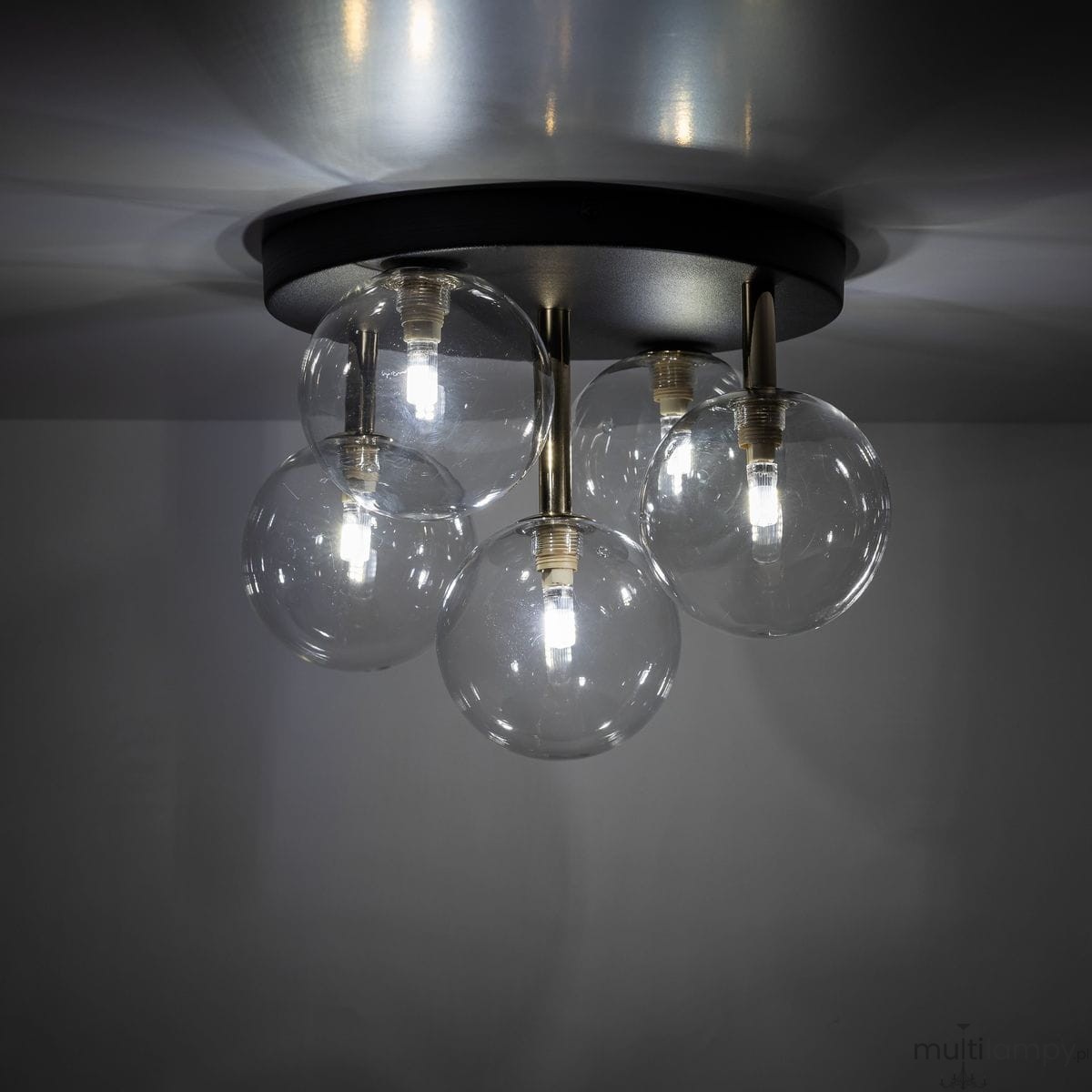 Lampa sufitowa Nilos z pięcioma kulistymi kloszami w przezroczystym kolorze, zamocowana na okrągłej czarnej podstawie. Wewnątrz kloszy znajdują się żarówki G9. Ujęcie z dołu, ukazujące szczegóły konstrukcji i źródła światła.