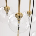 Lampa wisząca Nilos z 10 źródłami światła G9, czarna i transparentna. Widać szklane klosze w formie kul, złote mocowanie oraz czarne przewody. Produkt zawieszony w pionie, prezentujący nowoczesny design.