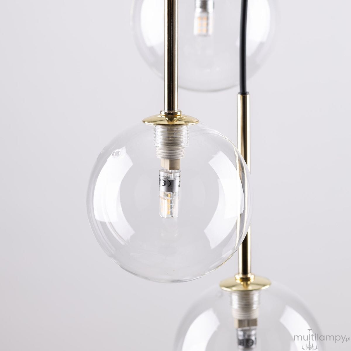 Lampa wisząca Nilos z siedmioma przezroczystymi kloszami w kształcie kul, zawieszona na złotych mocowaniach. Widać gwinty G9, w których umieszczone są źródła światła. Tło jasne, podkreślające elegancki design.