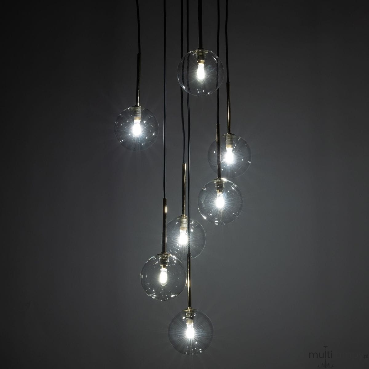 Lampa wisząca Nilos z siedmioma przezroczystymi kloszami, zawieszona na czarnych przewodach. Klosze mają okrągły kształt, a w środku znajdują się żarówki G9. Całość prezentuje nowoczesny design na ciemnym tle.