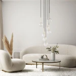 Lampa wisząca Nilos z siedmioma przezroczystymi kulami na czarnych przewodach, zawieszona nad okrągłym stołem w jasnym wnętrzu. Obok widać jasne sofy i dekoracyjne rośliny w wazonie.