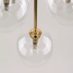 Lampa wisząca Nilos w kolorze czarnym i transparentnym, z pięcioma kulistymi kloszami. Widoczny złoty element mocujący i żarówki LED w szklanych kloszach. Ujęcie z góry, eksponujące detale konstrukcji i przezroczystość kloszy.