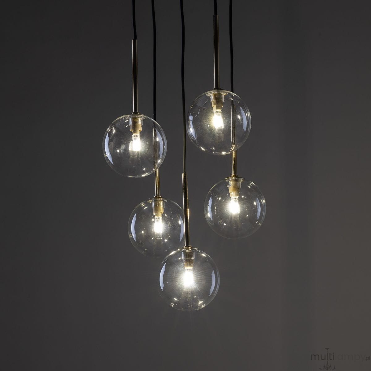 Lampa wisząca Nilos z pięcioma przezroczystymi kulami, zawieszona na czarnych linkach. Kule mają złote mocowania, w każdej znajduje się żarówka G9. Tło ciemne, podkreślające elegancki design lampy.