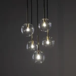 Lampa wisząca Nilos z pięcioma przezroczystymi kulami, zawieszona na czarnych linkach. Kule mają złote mocowania, w każdej znajduje się żarówka G9. Tło ciemne, podkreślające elegancki design lampy.