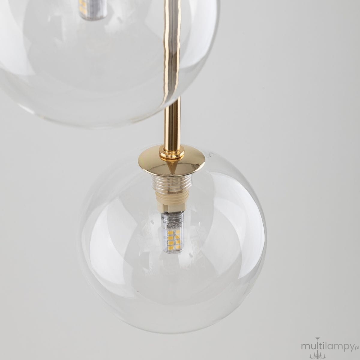 Lampa wisząca Nilos z trzema kloszami G9 w kolorze czarnym i transparentnym. Klosze w kształcie kul, wykonane ze szkła, z widocznymi żarówkami LED i złotym mocowaniem. Ujęcie z góry, ukazujące detale konstrukcji.