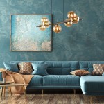 Lampa wisząca Estera z siedmioma żarówkami G9, w kolorze brązowym i bursztynowym. Zawieszona na długim, ciemnym stelażu, z okrągłymi kloszami, emitującymi ciepłe światło. Umieszczona w nowoczesnym wnętrzu z niebieską sofą i obrazem na ścianie.