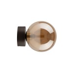 Kinkiet Estera 1xG9 w kolorze brązowym z bursztynową, okrągłą kloszem. Produkt montowany na ścianie, z metalowym elementem mocującym w kolorze czarnym. Klosz transparentny, o gładkiej fakturze, z widocznym źródłem światła wewnątrz.