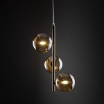 Lampa wisząca Estera z trzema kulami w kolorze złotym i bursztynowym, zawieszona na cienkim przewodzie. Kule o gładkiej powierzchni odbijają światło, a smukły metalowy element w centrum podkreśla nowoczesny design.