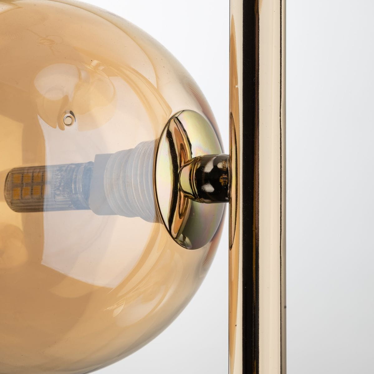 Lampa wisząca Estera 3xG9 w złotym wykończeniu z bursztynowymi kloszami. Zbliżenie na klosz z przezroczystego szkła, metalowa oprawa z połyskującym wykończeniem. Widoczny gwint żarówki w środku klosza.