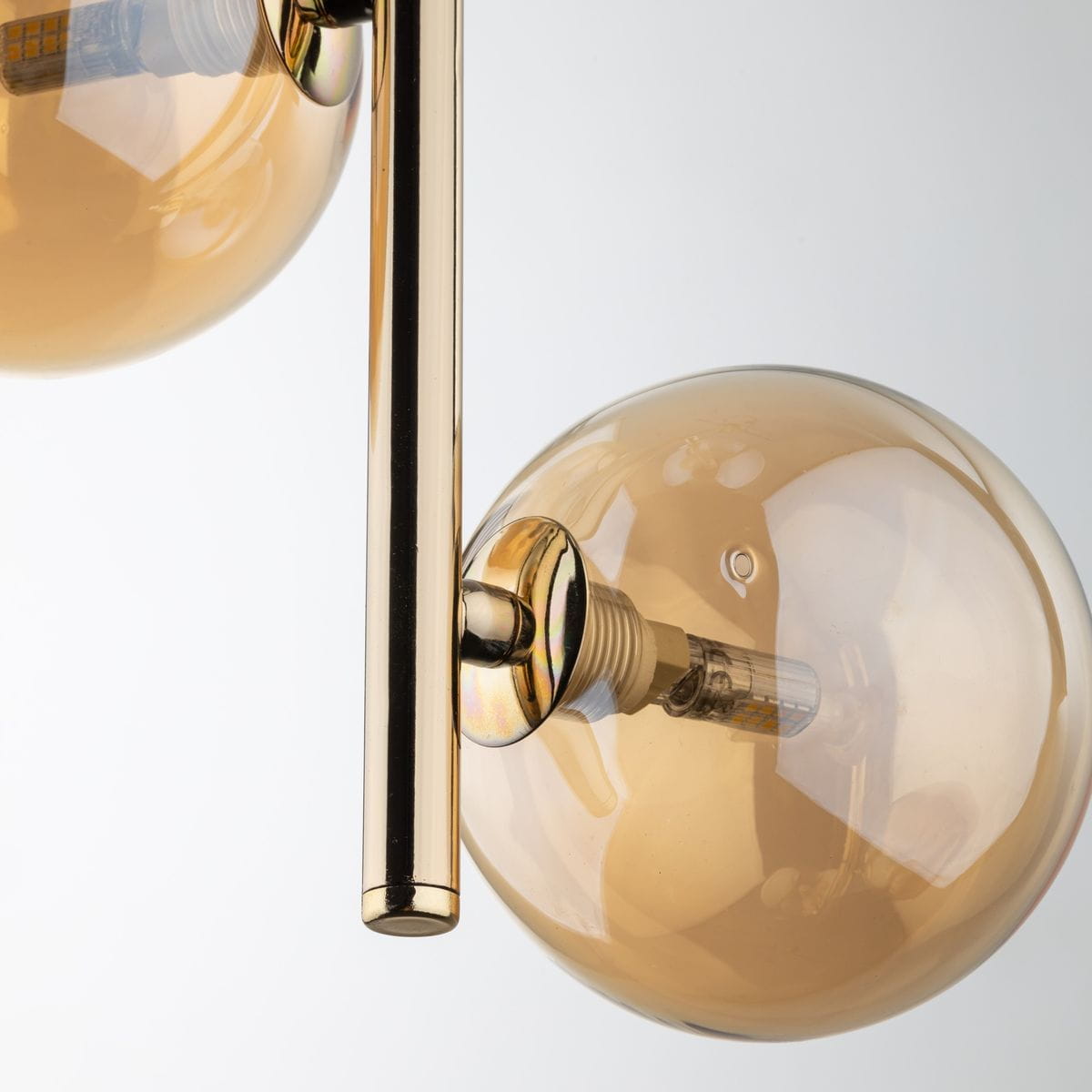 Lampa wisząca Estera 3xG9 w kolorze złotym i bursztynowym, z przezroczystymi, szklanymi kloszami w kształcie kul. Ujęcie zbliżeniowe na detale mocowania i żarówki, z metalowym elementem w kolorze złotym.