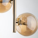 Lampa wisząca Estera 3xG9 w kolorze złotym i bursztynowym, z przezroczystymi, szklanymi kloszami w kształcie kul. Ujęcie zbliżeniowe na detale mocowania i żarówki, z metalowym elementem w kolorze złotym.