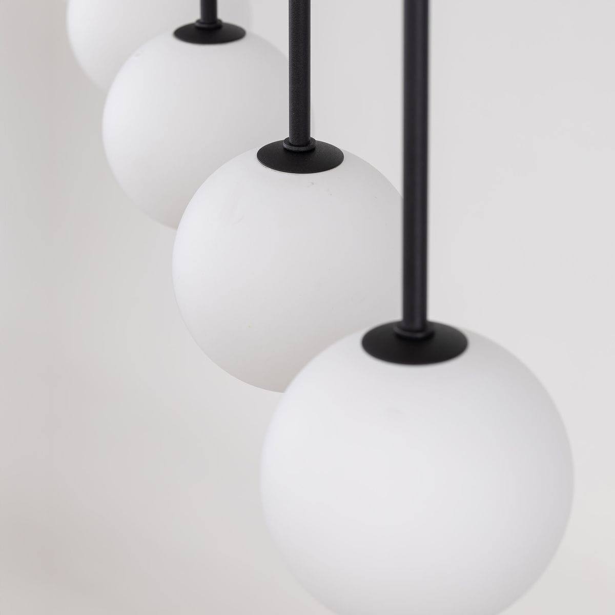 Czarna lampa wisząca Martin z czterema kulistymi kloszami z matowego szkła. Klosze zawieszone na cienkich, czarnych rurkach. Ujęcie zbliżone, prezentujące detale kloszy i ich mocowania.
