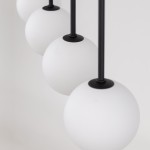 Czarna lampa wisząca Martin z czterema kulistymi kloszami z matowego szkła. Klosze zawieszone na cienkich, czarnych rurkach. Ujęcie zbliżone, prezentujące detale kloszy i ich mocowania.