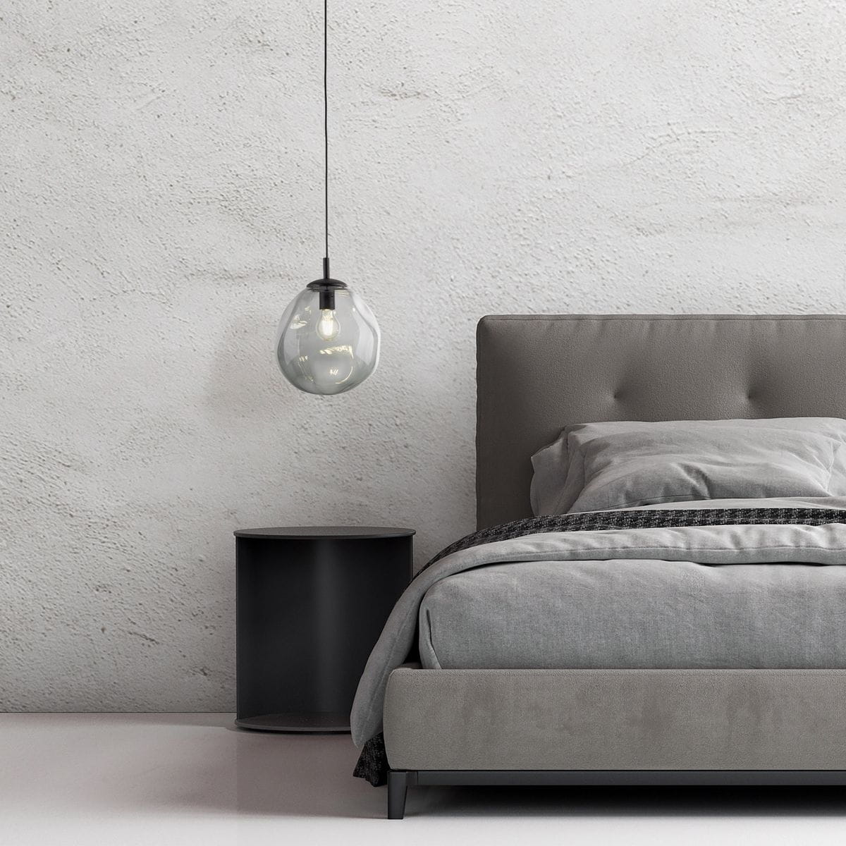 Lampa wisząca Sol D25 z żarówką E27 w kolorze czarnym i grafitowym. Okrągły, przezroczysty klosz w kształcie kropli zawieszony na cienkim przewodzie. Widoczna w aranżacji sypialni, nad szarym łóżkiem i nocnym stolikiem.