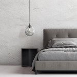 Lampa wisząca Sol D25 z żarówką E27 w kolorze czarnym i grafitowym. Okrągły, przezroczysty klosz w kształcie kropli zawieszony na cienkim przewodzie. Widoczna w aranżacji sypialni, nad szarym łóżkiem i nocnym stolikiem.