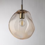 Lampa wisząca Sol D25 w kolorze bursztynowym z metalowym detalem w złotym wykończeniu. Owalny klosz z przezroczystego szkła, zawiera żarówkę E27. Produkt zawieszony na czarnym przewodzie, prezentowany na jasnym tle.