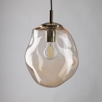 Lampa wisząca Sol D25 z kloszem w bursztynowym kolorze, wykonana z przezroczystego szkła. U podstawy złoty element mocujący z oprawką na żarówkę E27. Produkt zwisający na czarnym przewodzie, prezentujący nowoczesny design.