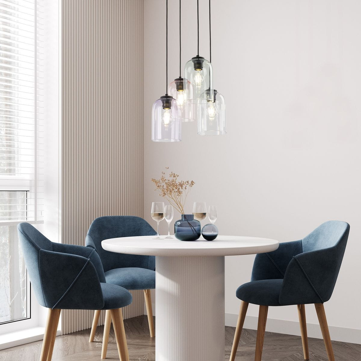 Lampa wisząca Molly z czterema kloszami w różnych kolorach, zawieszona na czarnych przewodach. Klosze mają różne kształty, a lampa znajduje się nad okrągłym białym stołem w nowoczesnym wnętrzu z niebieskimi krzesłami.