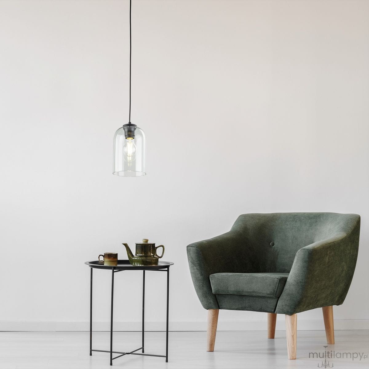 Czarna lampa wisząca Molly z kloszem w kształcie dzwonu, zawieszona na czarnym przewodzie. W tle zielony fotel oraz okrągły stolik z zestawem filiżanek i czajniczkiem. Proste, jasne tło. Lampa z jedną oprawą E27.