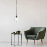 Czarna lampa wisząca Molly z kloszem w kształcie dzwonu, zawieszona na czarnym przewodzie. W tle zielony fotel oraz okrągły stolik z zestawem filiżanek i czajniczkiem. Proste, jasne tło. Lampa z jedną oprawą E27.