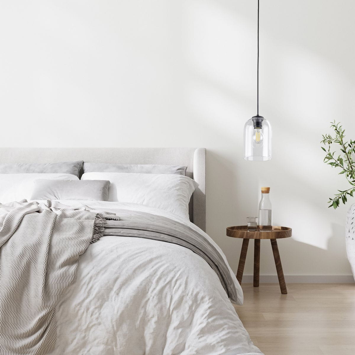 Lampa wisząca Molly 1xE27 w kolorze czarnym i transparentnym, zawieszona nad łóżkiem, z przezroczystym kloszem i czarnym mocowaniem. W tle widoczna jasna ściana oraz eleganckie meble w neutralnych kolorach.