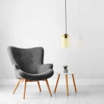 Lampa wisząca Molly w kolorze czarnym i żółtym, z przezroczystym kloszem, zawieszona na czarnym przewodzie. W tle szare krzesło i biały stolik z rośliną, na jasnym tle.