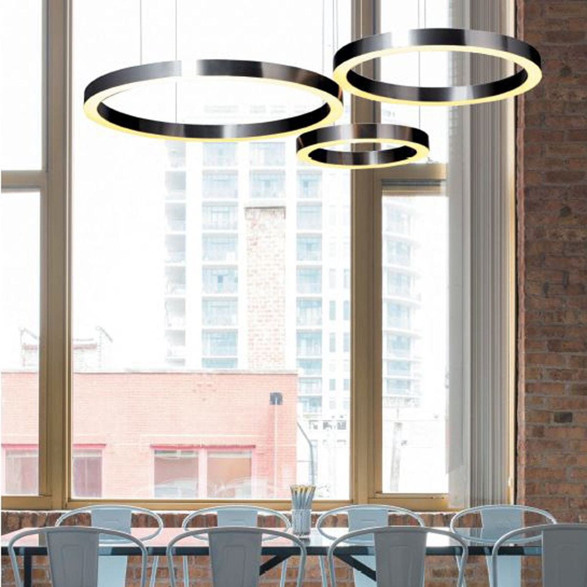 Lampa wisząca Circle D80 w kolorze niklowym, składająca się z trzech okrągłych pierścieni LED. Zawieszona w nowoczesnym wnętrzu, na tle dużych okien. Dwa źródła światła 40W, z możliwością sterowania pilotem.