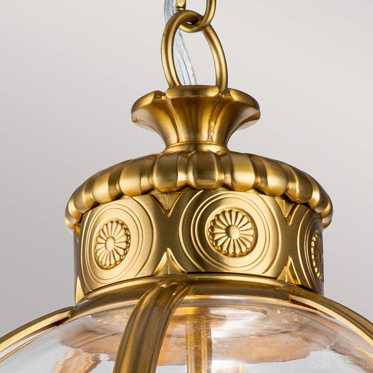 Mosiężna lampa wisząca Adams z trzema gniazdami E14, z ozdobnym kloszem i detalami w formie kwiatowych wzorów. Ujęcie z góry, ukazujące dekoracyjny element mocowania oraz przezroczysty klosz.