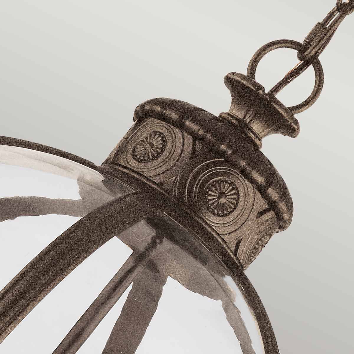 Lampa wisząca Adams w kolorze antycznego brązu z trzema oprawami E14. Widoczna metalowa podsufitka z dekoracyjnym wzorem oraz szklany klosz, zawieszona na łańcuchu, w ujęciu z góry.