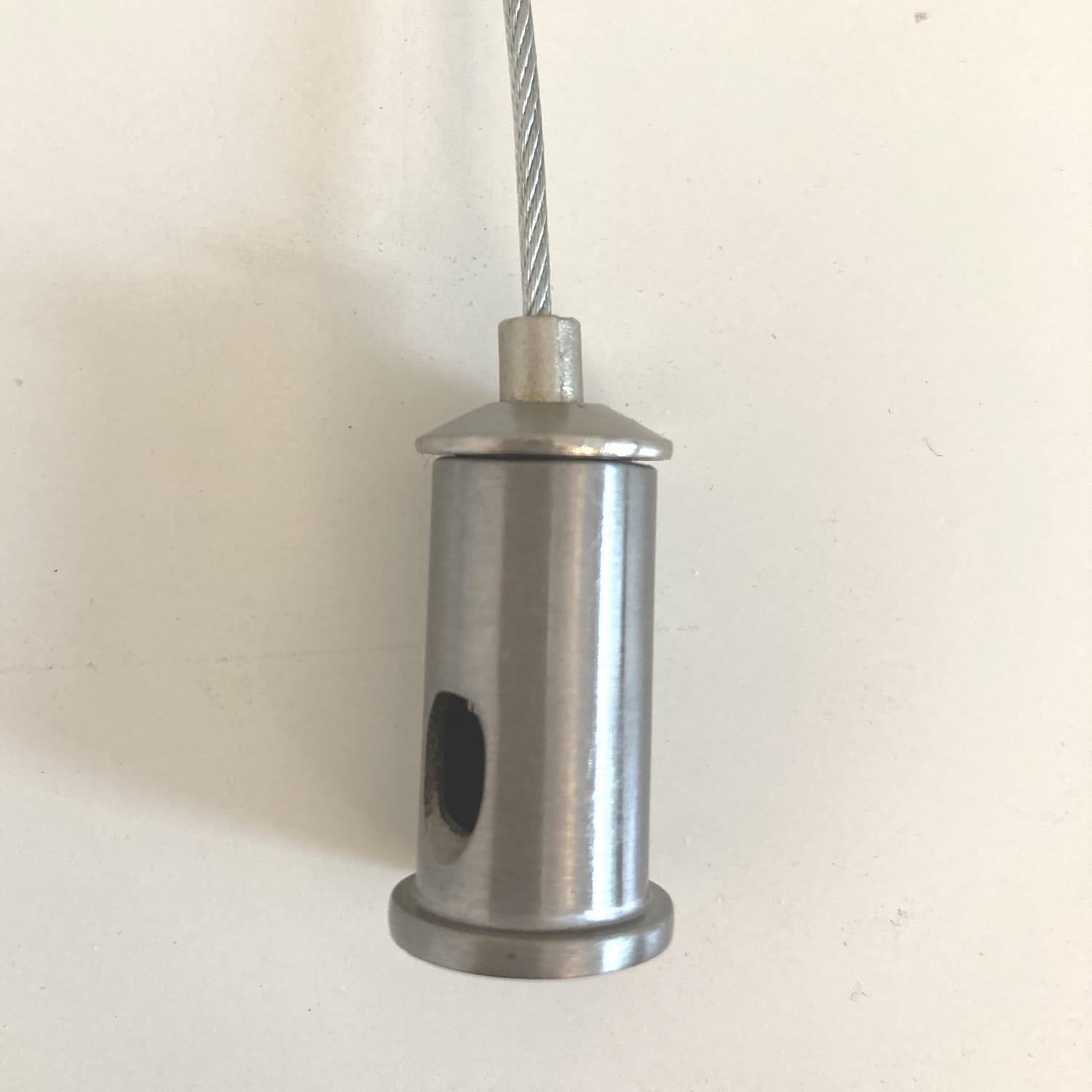 Detal uchwytu lampy wiszącej Circle 40+60+80, wykonany z niklu. Cylindryczny kształt z widocznym otworem, zakończony okrągłą podstawą. Element zawieszony na stalowym drucie, idealny do nowoczesnych aranżacji oświetleniowych.
