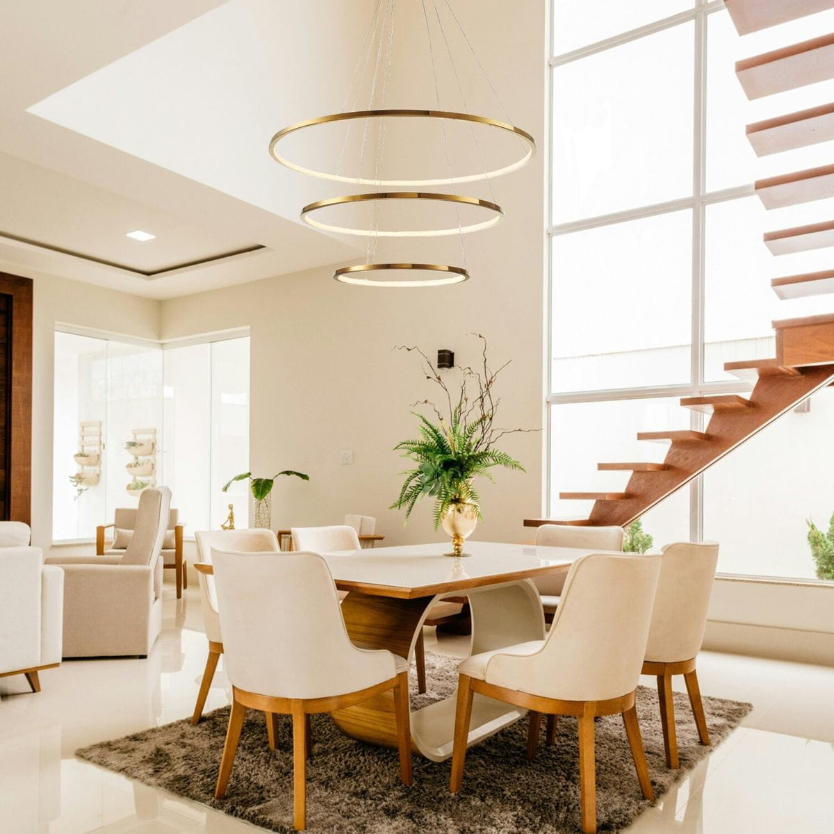 Lampa wisząca Circle Slim 40+60+80 l z trzema złotymi pierścieniami oświetleniowymi, zawieszona nad stołem w jadalni. W tle widać drewniane schody i rośliny w eleganckim wnętrzu.