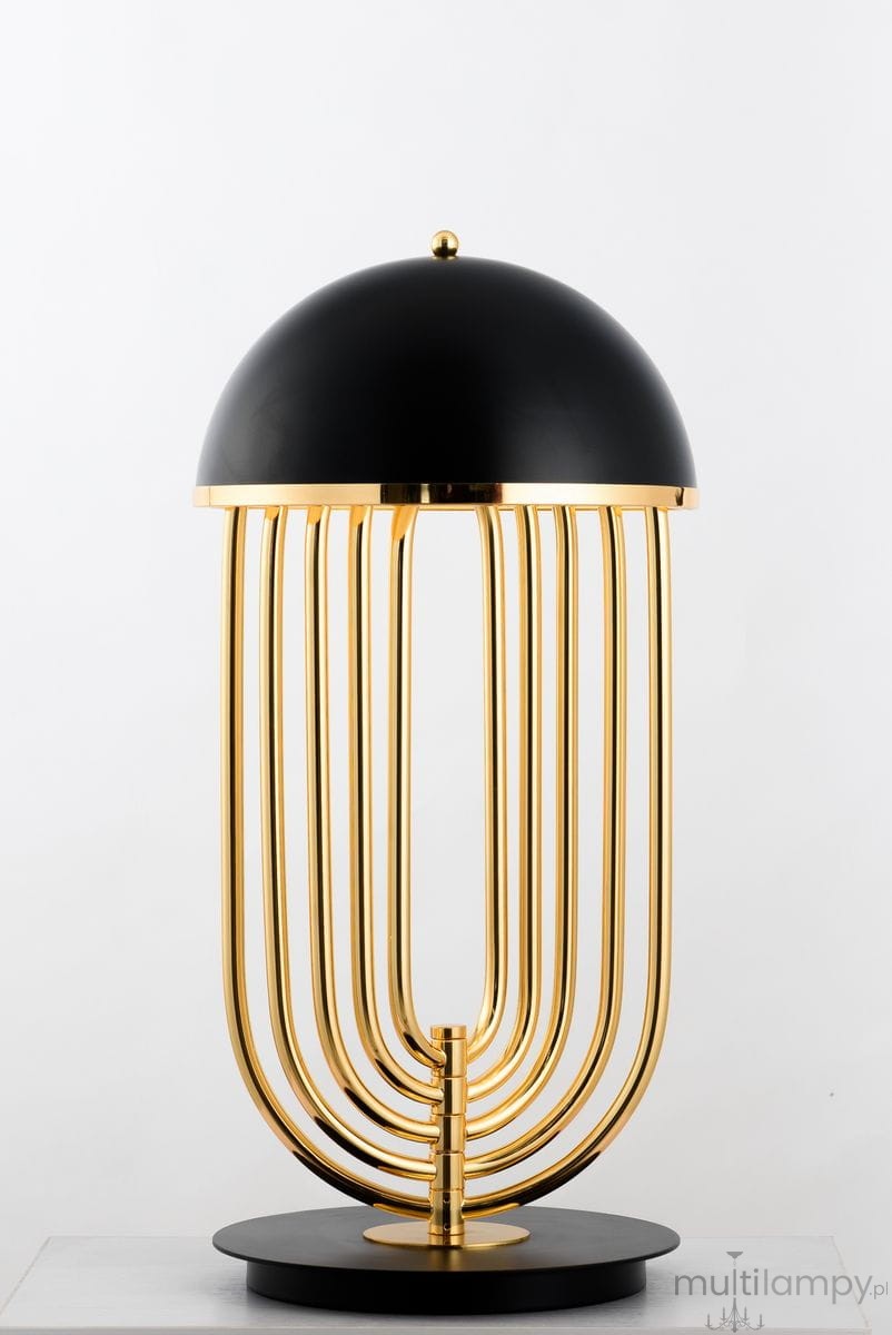 Lampa stołowa Dolce Vita, czarna ze złotymi elementami, o zaokrąglonym kloszu i ośmiu złotych prętach tworzących podstawę. Ujęcie frontalne, produkt stojący na okrągłej podstawie.