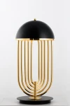 Lampa stołowa Dolce Vita, czarna ze złotymi elementami, o zaokrąglonym kloszu i ośmiu złotych prętach tworzących podstawę. Ujęcie frontalne, produkt stojący na okrągłej podstawie.
